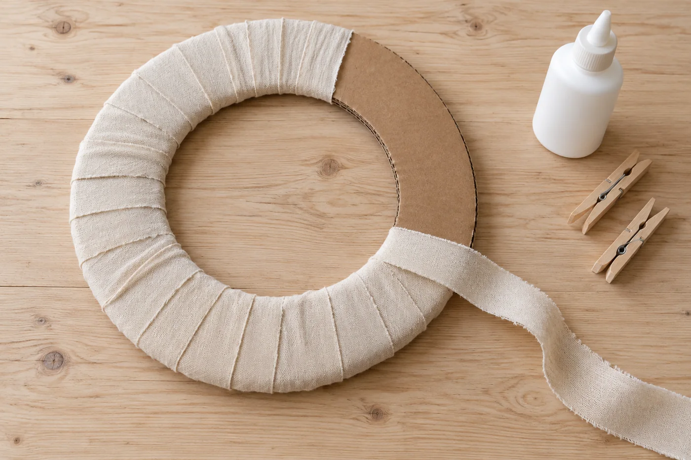 Argola de papelão parcialmente revestida com tiras de tecido bege sobrepostas